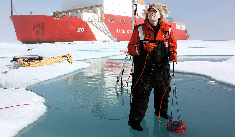 Professor Karen Frey standing on ice with Coast Guard ship behind he
