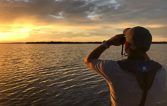 Man with binoculars looking at sunset over ocean