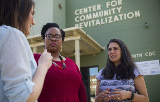 Laurie Ross st和ing with community partners in front of a building marked 'Center for Community Revitalization.'