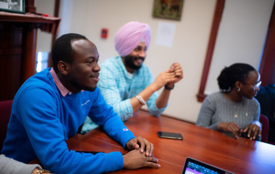 Students smiling, seated in a seminar classroom in the Department of Sustainability and Social Justice