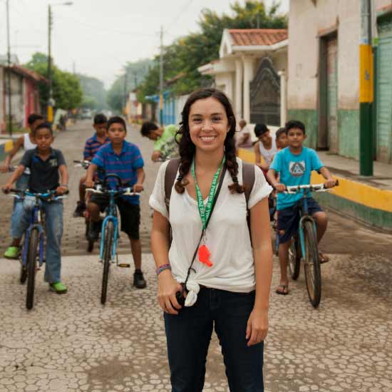 "A Peace Corps volunteer in a cobblestone road flanked by children on bicycles.