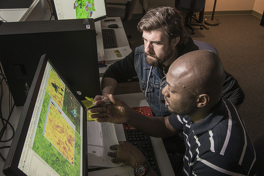 professor and graduate student looking over maps on pc