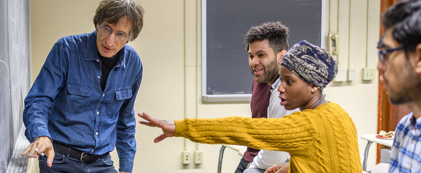 students in class pointing to chaulk board with professor