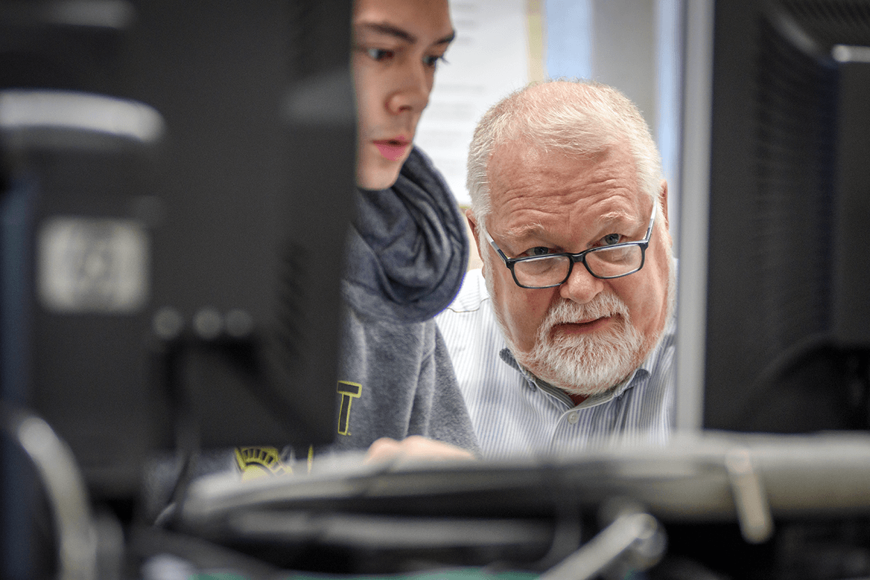 Image of student and faculty member looking at a monitor, working in a computer lab.