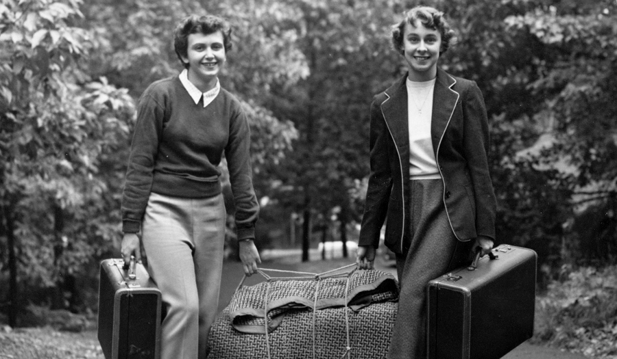Two women carrying suitcases on campus