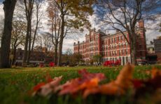A close-up of fall leaves on grass in the foreground with Jonas Clark Hall in the distance
