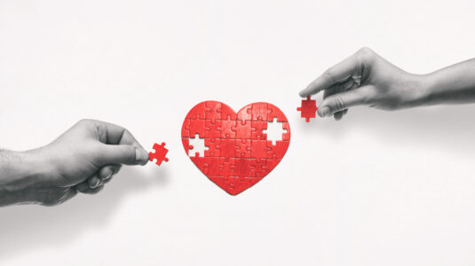 hands putting together heart-shaped puzzle