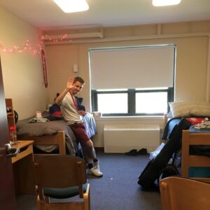 Ben DiFilippi, ‘21, MBA 22 sitting on a bed in a college dorm room