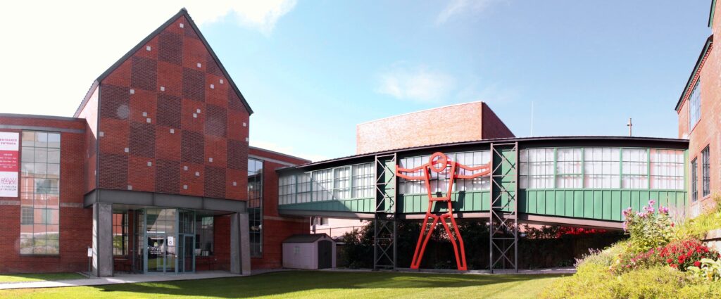 Front facade of the Fitchburg art museum - brick building with glass walkway and sculptural person supporting walls