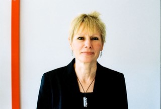 Smiling woman with blond hair wearing a black jacket and necklace.
