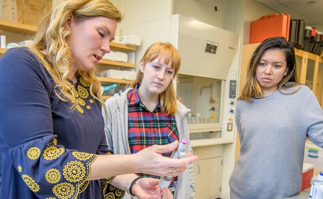 Researcher in lab showing samples to two students