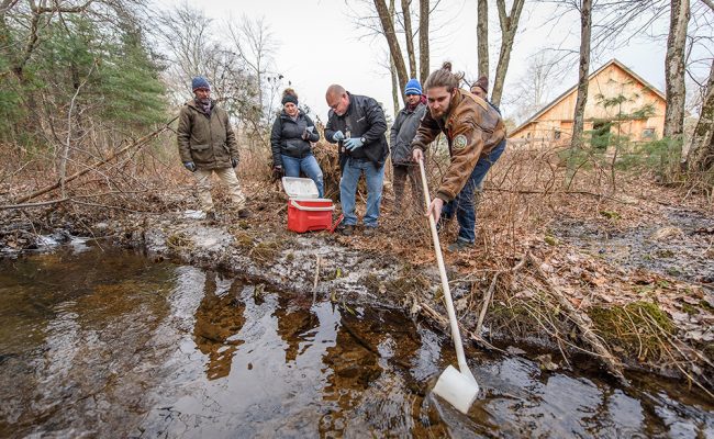 Four researchers gathering water samples from pond