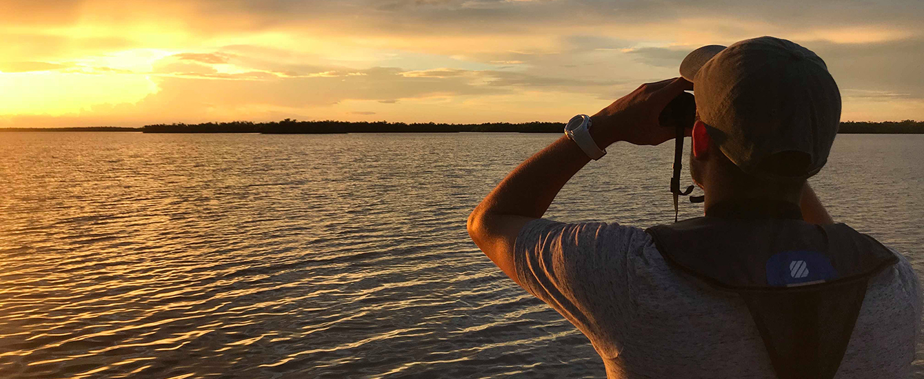 Man using binoculars to look at sunset over water