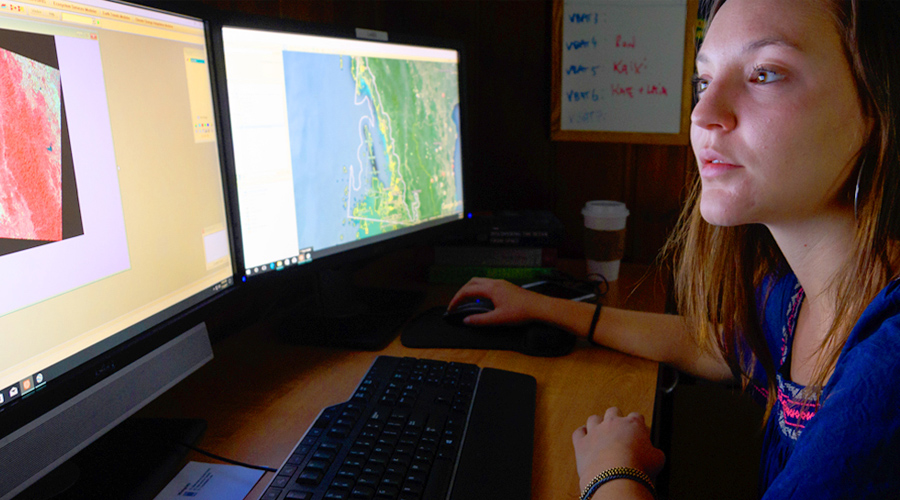 Girl sitting in front of two computer screens reviewing gis maps.