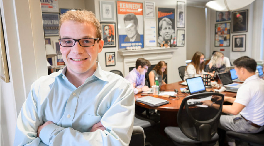 political science student posing for camera with other students in background at desk