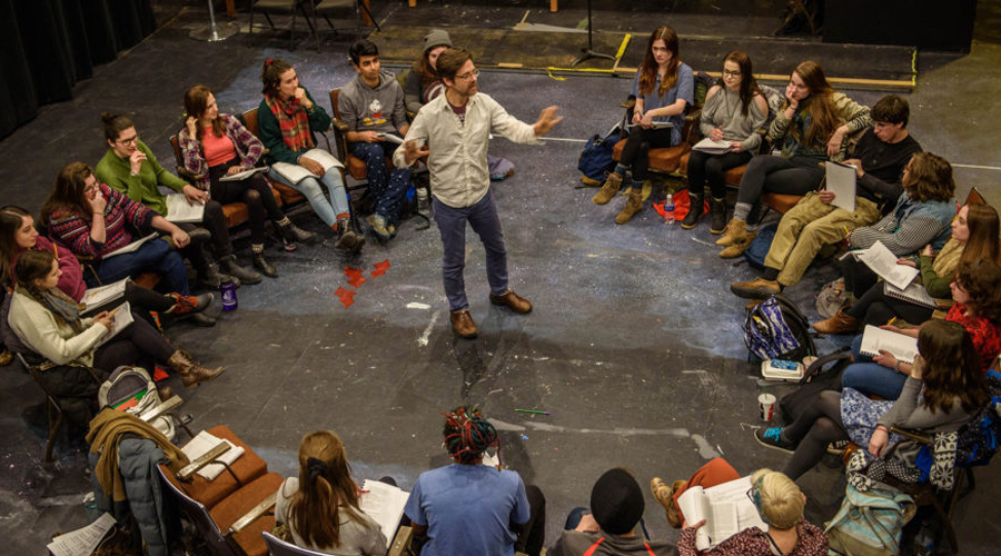 professor in theatre arts class surrounded by students on stage