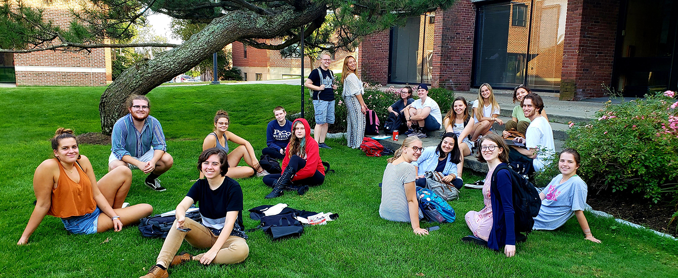 Students sitting on grass and standing outside in class
