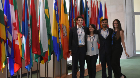 Four students stand in front of flags at United Nations