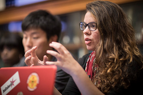 A Department of Sustainability and Social Justice student seated in front of a computer engaged in discussion.