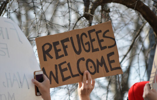 A person holding a homemade sign on cardboard that says 'refugees welcome'