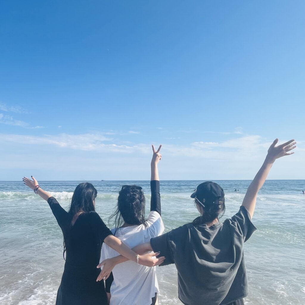 Shot from behind of three students waving at a beautiful ocean blue with clear sky.