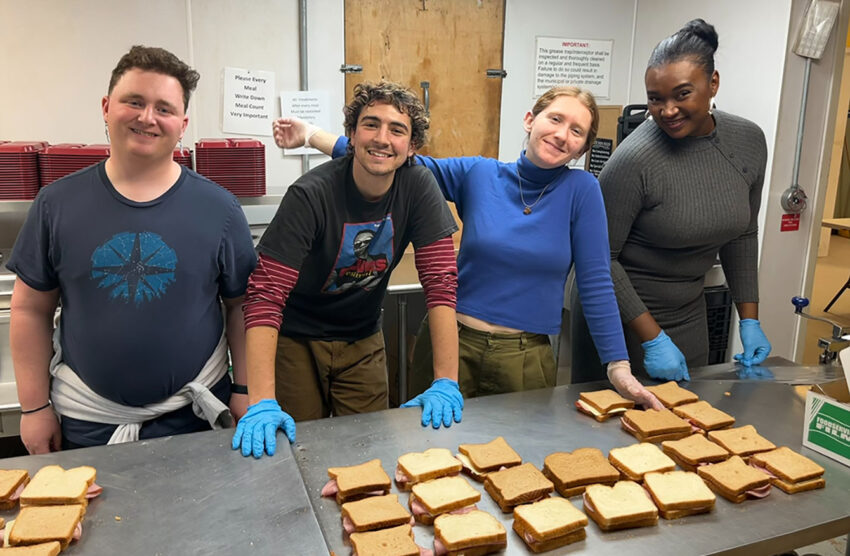 Four students pose, smiling while making sandwiches during alternative spring break