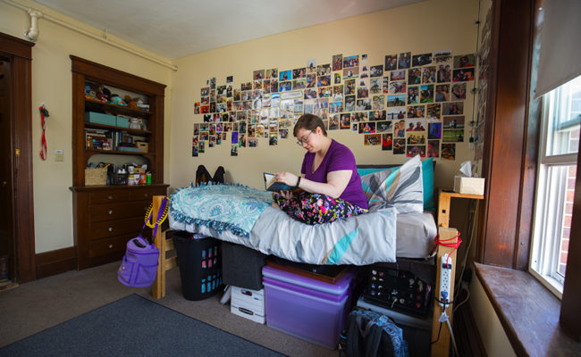 graduate housing: 926 Main St. Apartment Bedroom with woman sitting on bed reading boo