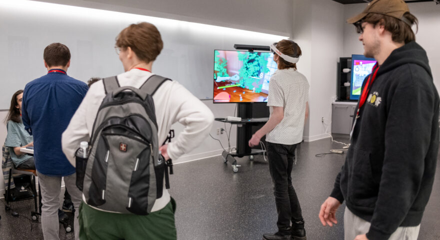 Group of people stand around a person in a virtual reality headset.