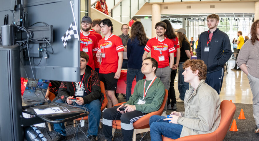 Group of people around large TV play a multiplayer video game.