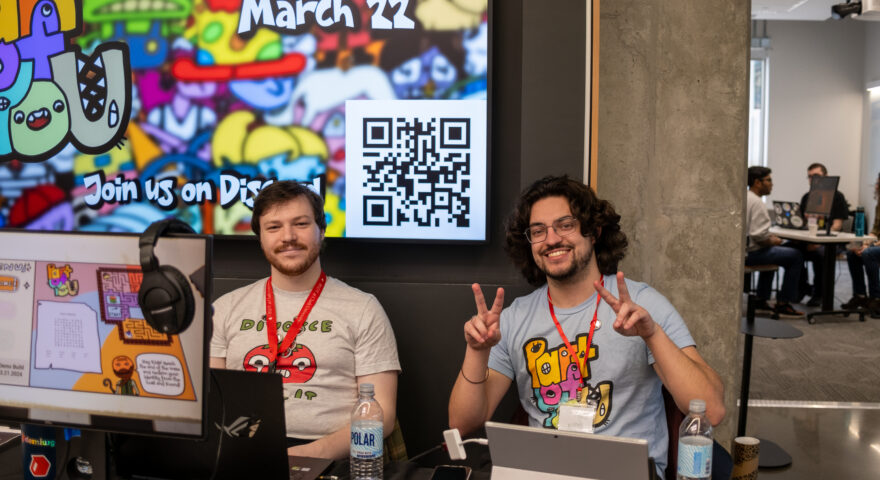 Two people sit behind video game display smiling.