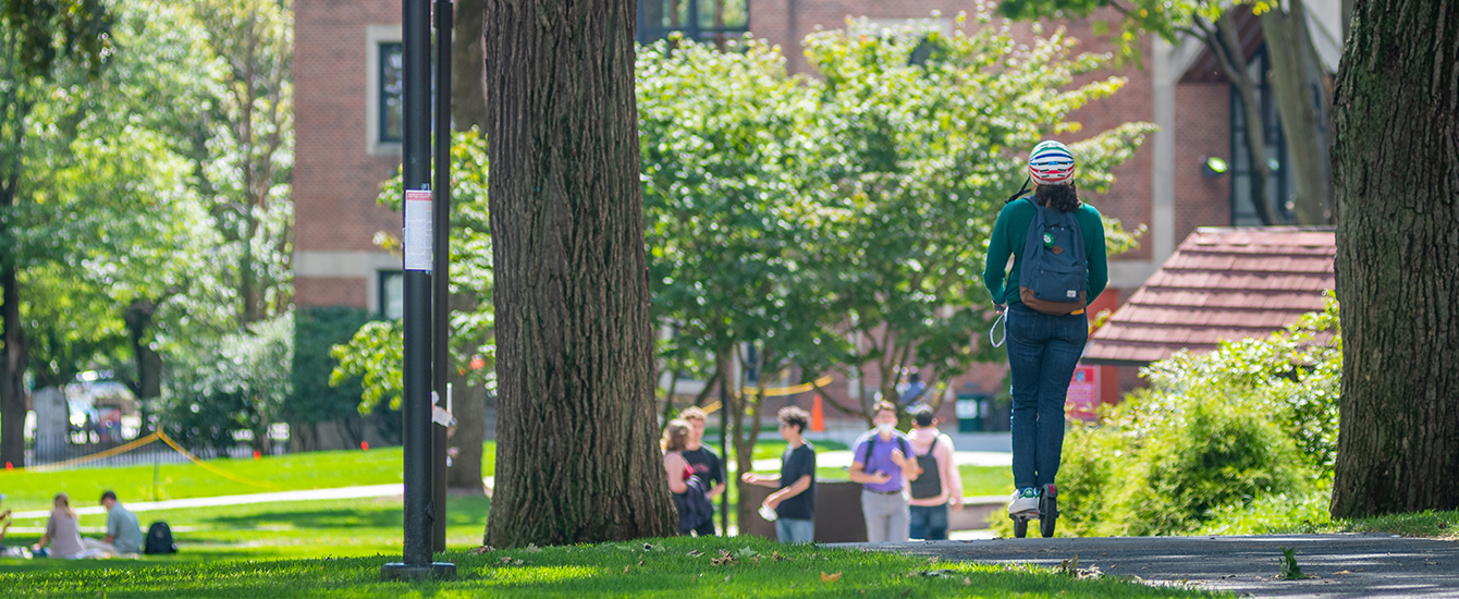 student on scooter going through campus green
