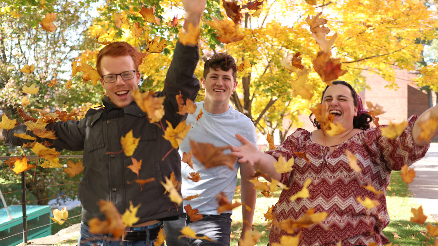 Three students playing in leaves on campus