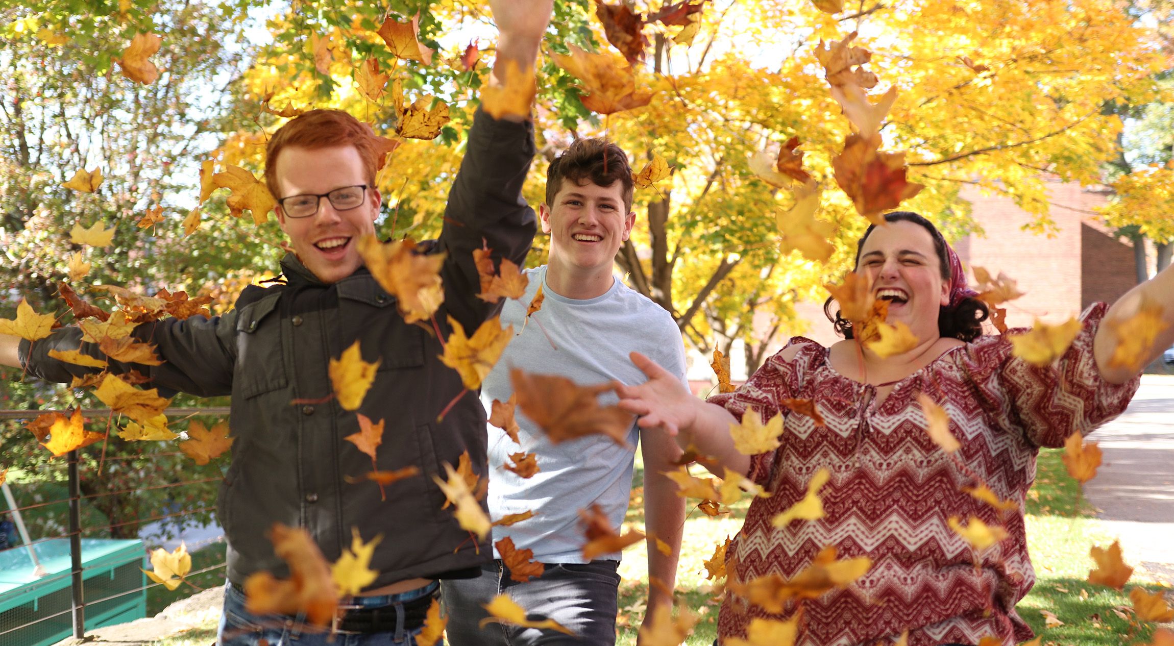Three students playing in leaves on campus