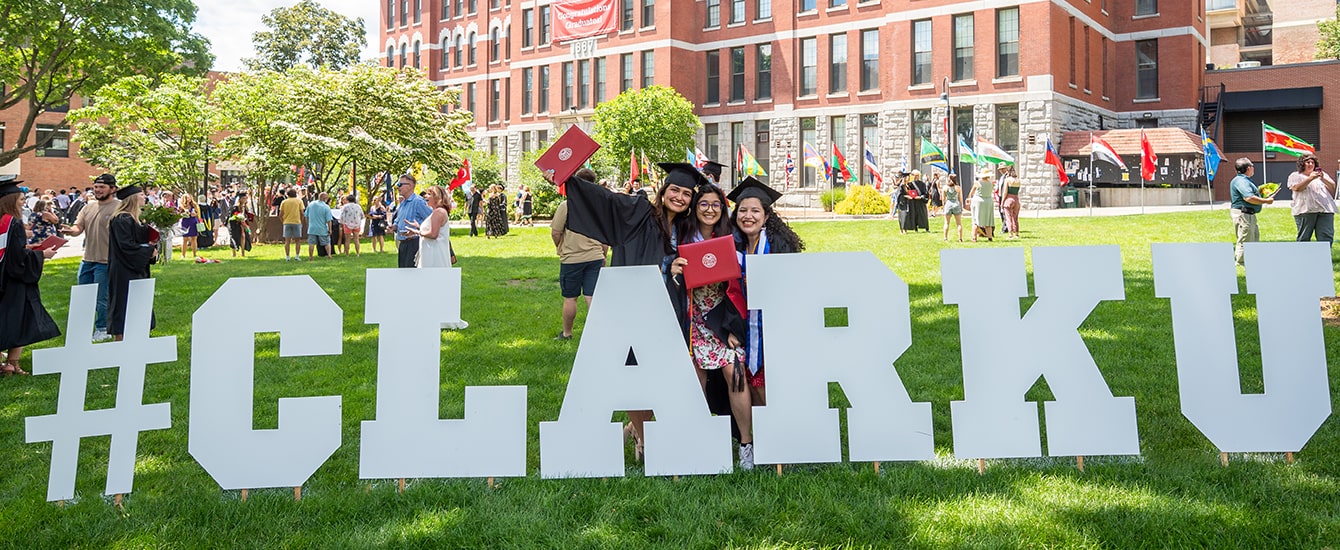 Students in cap and gown in front of Clark University sign