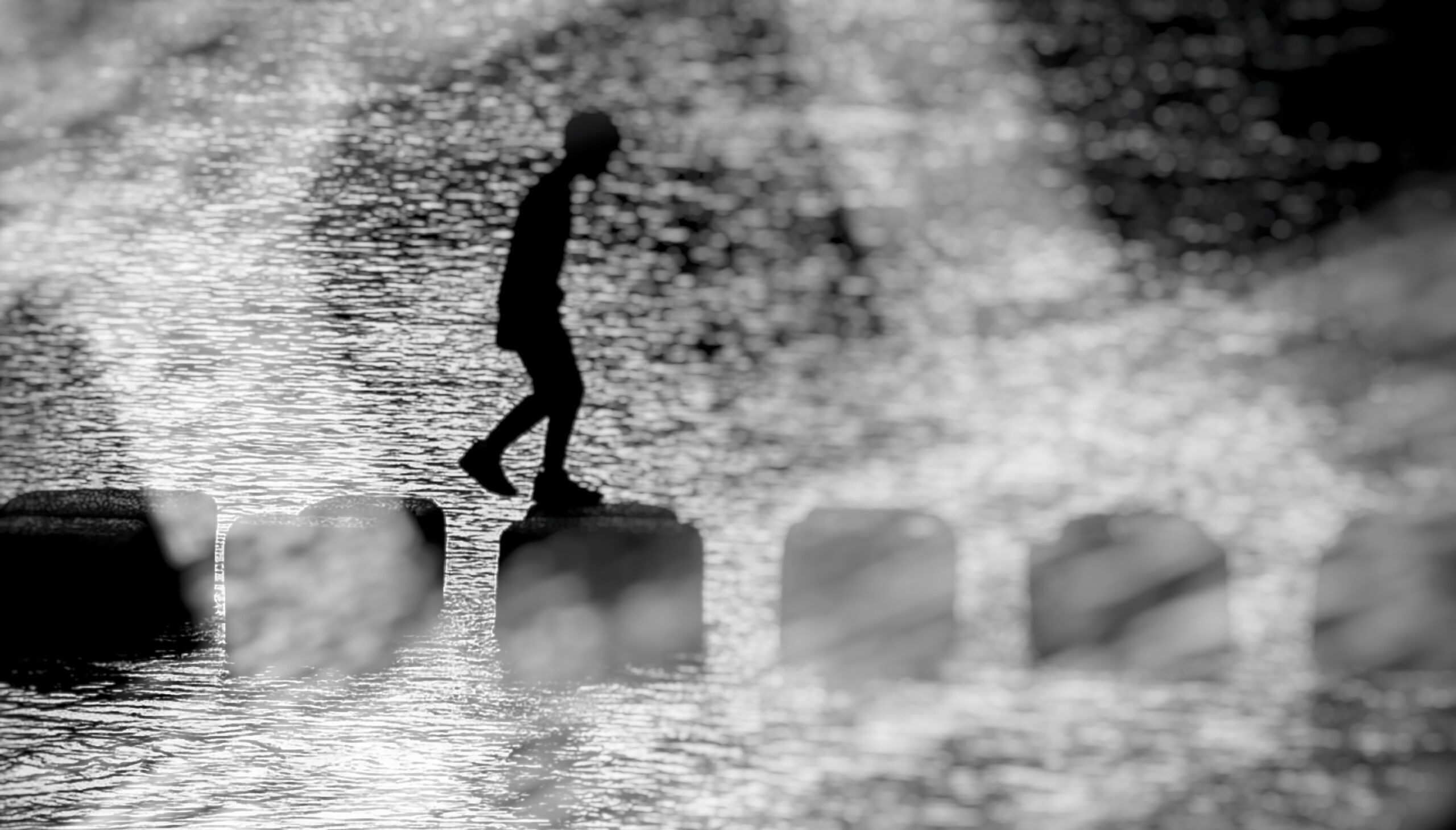 Black and white photo of a child walking on stone steps. The steps are surrounded by water.