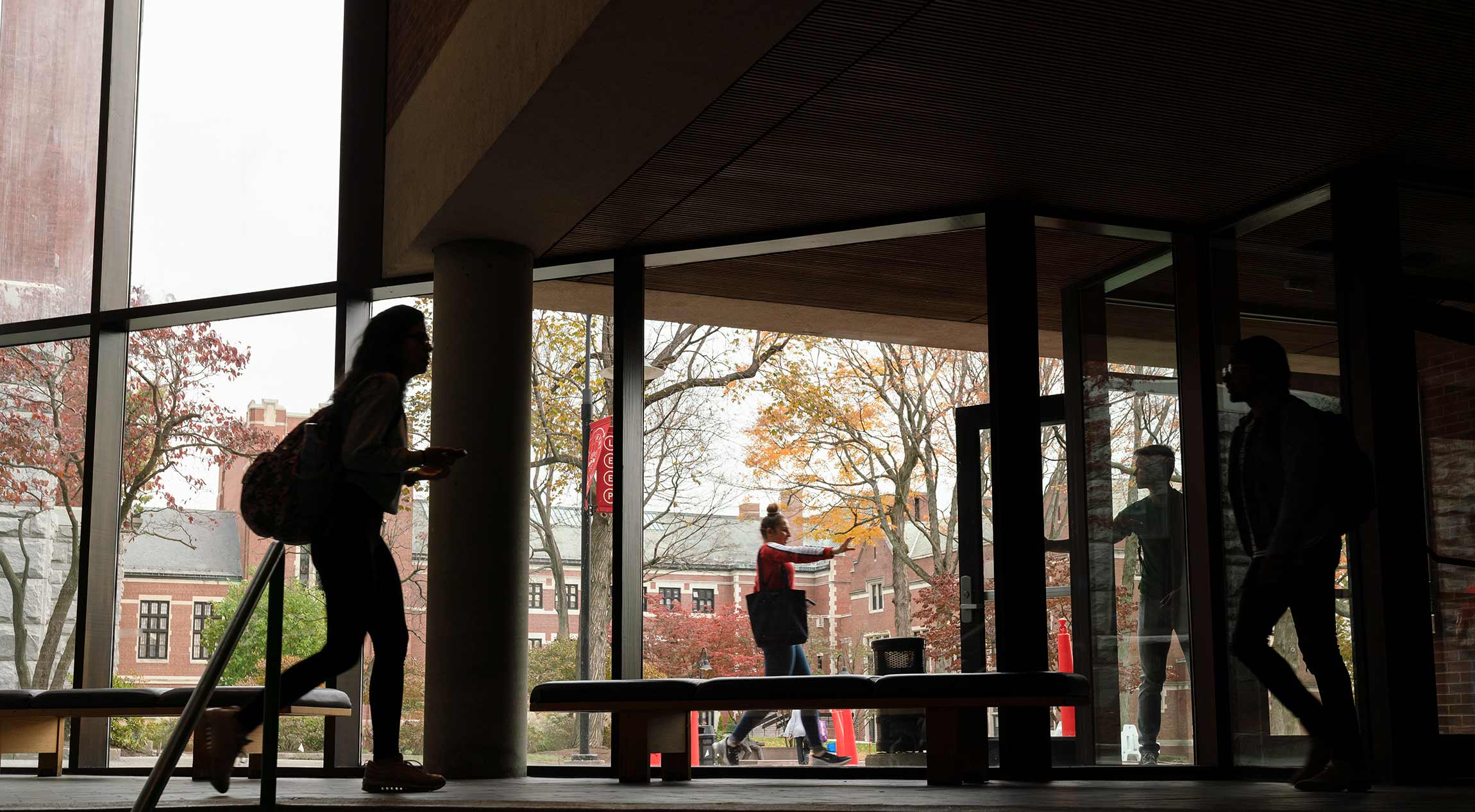 Students silhouetted against a large window facing onto the center of campus