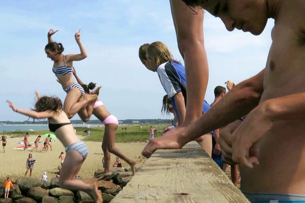 Image of people in bathing suits jumping from a wooden bridge