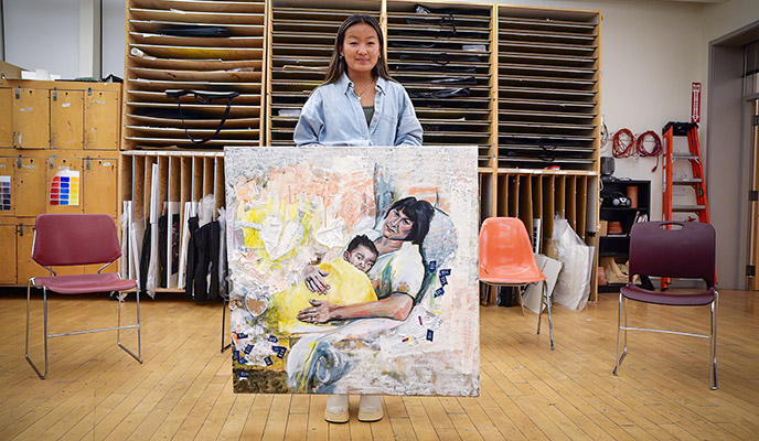 Wynne Dromey ’25, a double major in studio art and marketing with a minor in entrepreneurship and innovation standing in a studio with her painting, 'Embrace.'