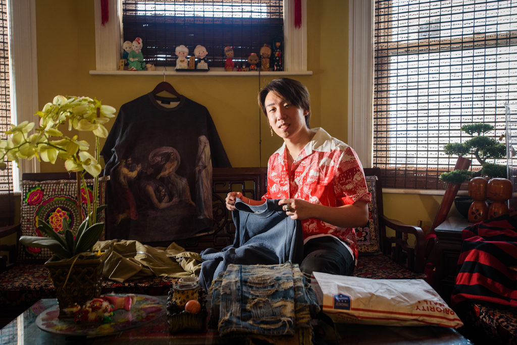 Kendrick Quek sits in his living room and holds up his vintage fashion