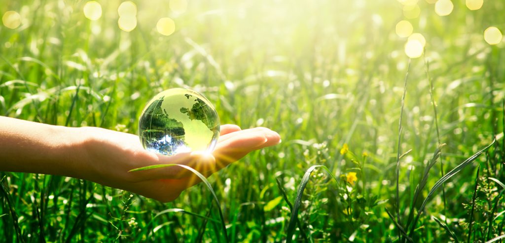 Earth Day - crystal glass globe in human hand on grass background. Saving environment and clean green planet concept. Card for World Earth Day concept.