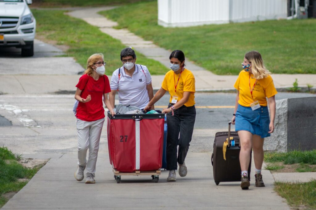 orientation leaders help students with red moving bin move onto campus