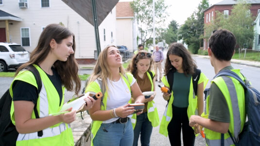 five students in green safety vests stand together while conducting research in a Worcester neighborho