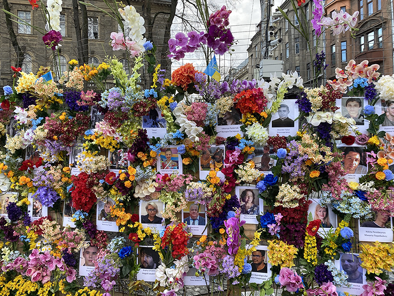 A memorial fence of flowers and photos of Ukrainian war victims.