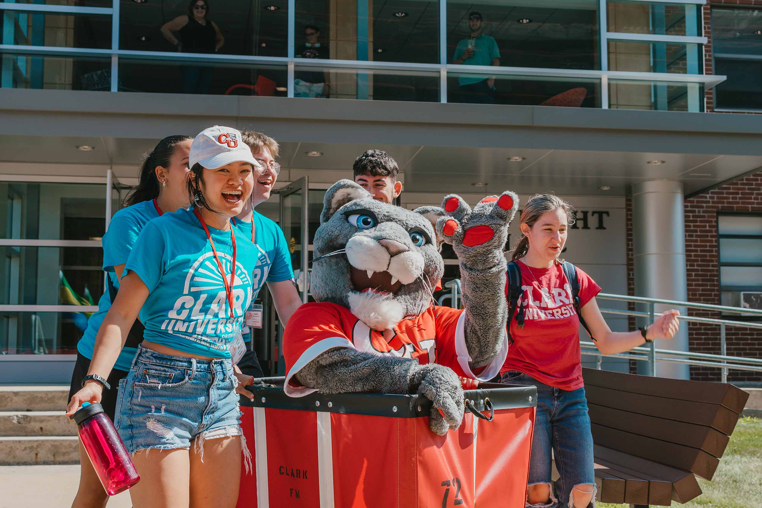Smiling students with the cougar mascot sitting in a rolling cart