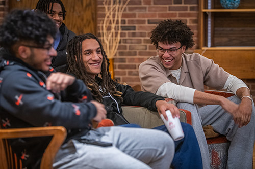 A group of students laughing and smiling during a gathering event of the Men of Color Alliance at Clark University