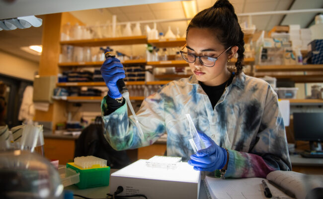 A student wearing a tie-dyed lab coat working with lab samples