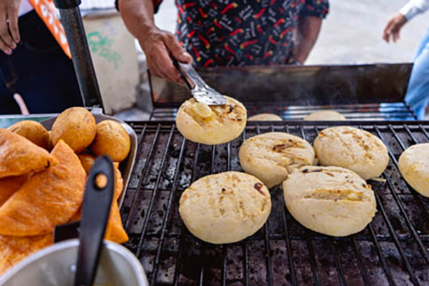 A person making arepas on an open grill.