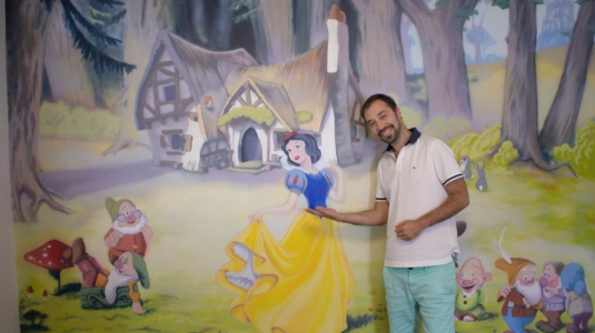 man standing in front of painted mural with Snow White scene.