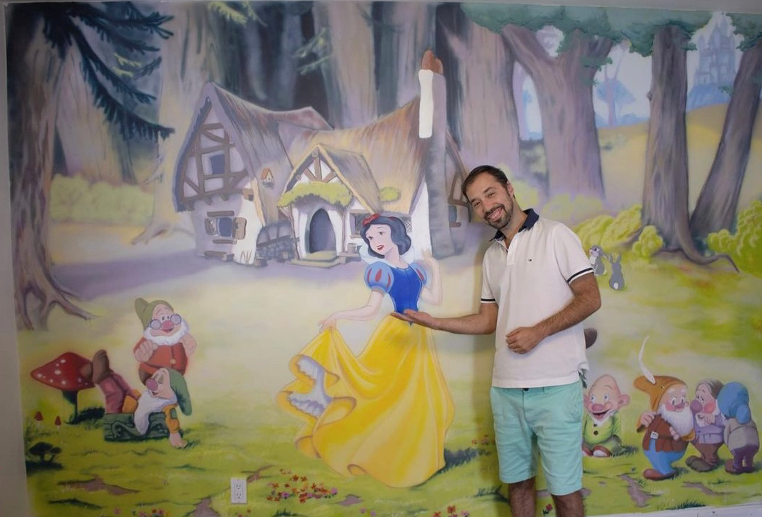 man standing in front of painted mural with Snow White scene.